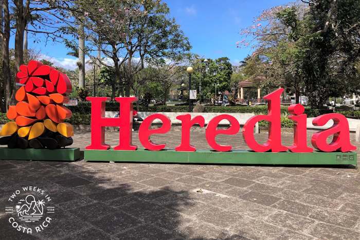 Large red letters spell Heredia on a sidewalk
