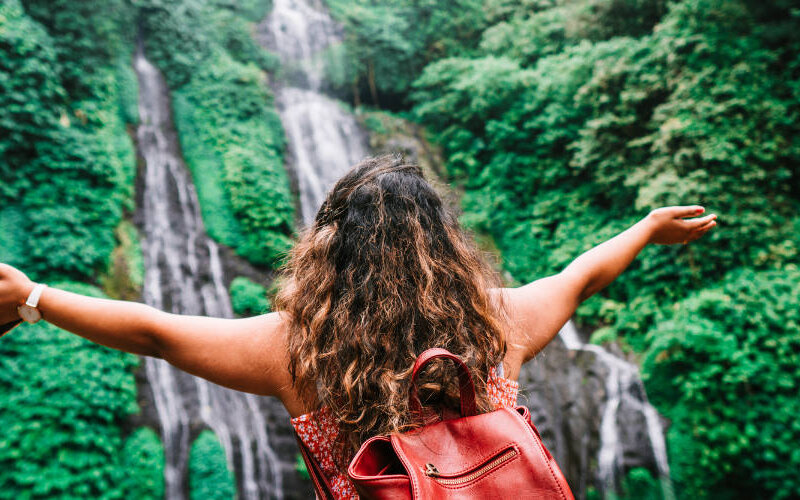 Woman with backpack facing waterfall with arms open