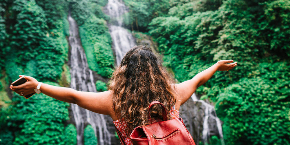 Woman with backpack facing waterfall with arms open